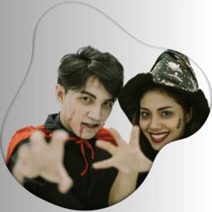 Young man in vampire costume with blood makeup and red cape, woman wearing witch hat and Halloween makeup